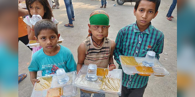 Three children holding food and drink trays outdoors, looking at the camera