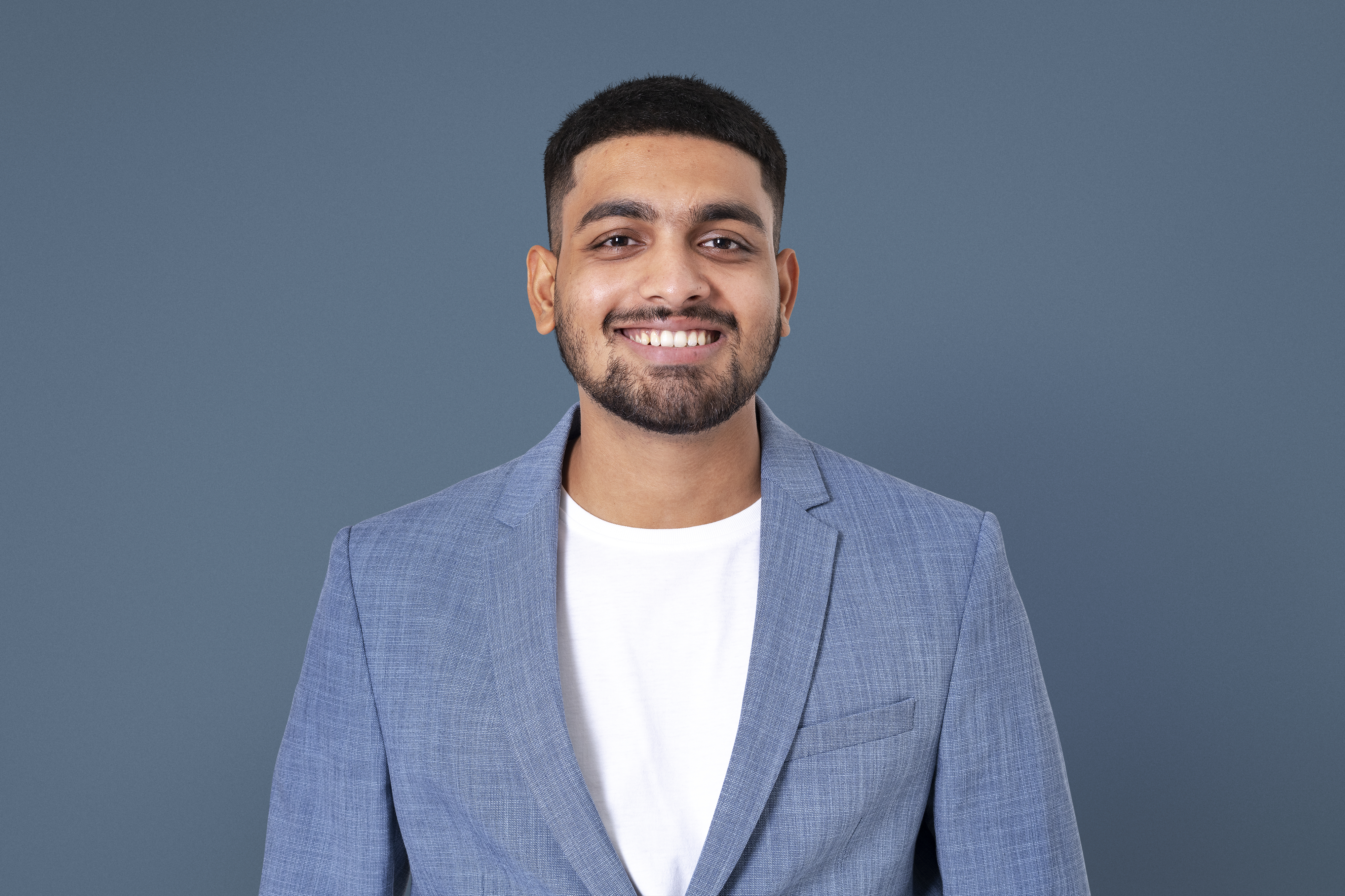 Smiling man in light blue blazer and white shirt against gray background